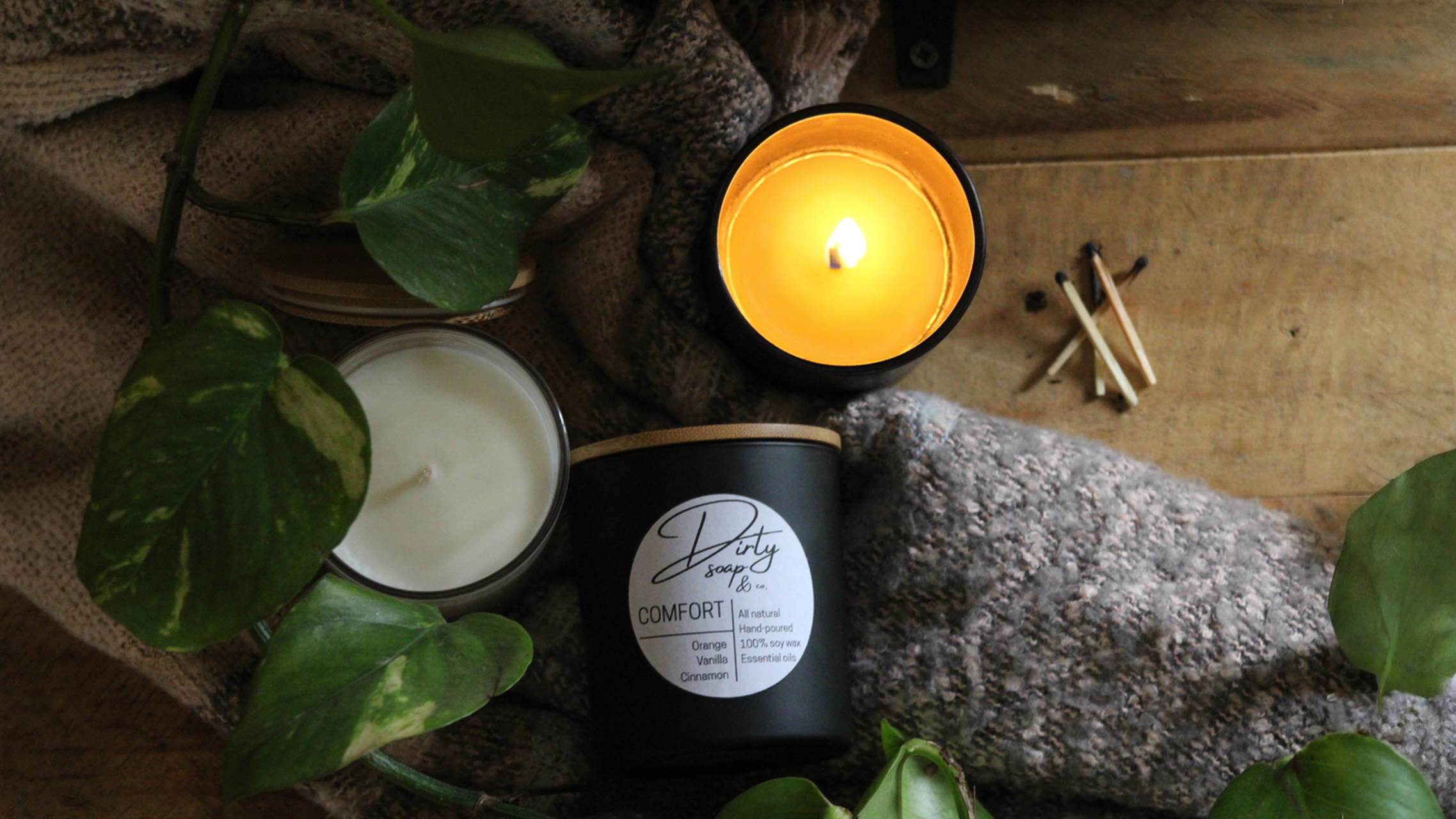 Three beautiful natural soy wax candles in glass containers with bamboo lids in a cozy home environment