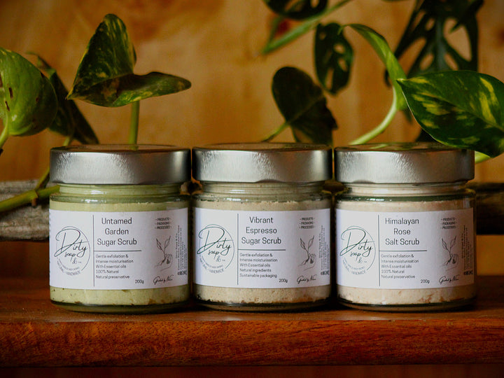 Range of three whipped body scrubs in glass jars with paper labels in natural inspired setting